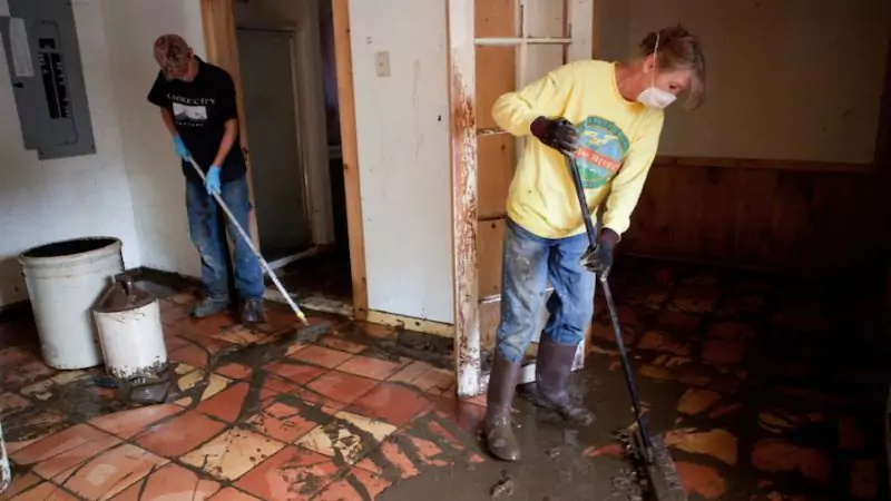 Two individuals cleaning a flooded room with mops