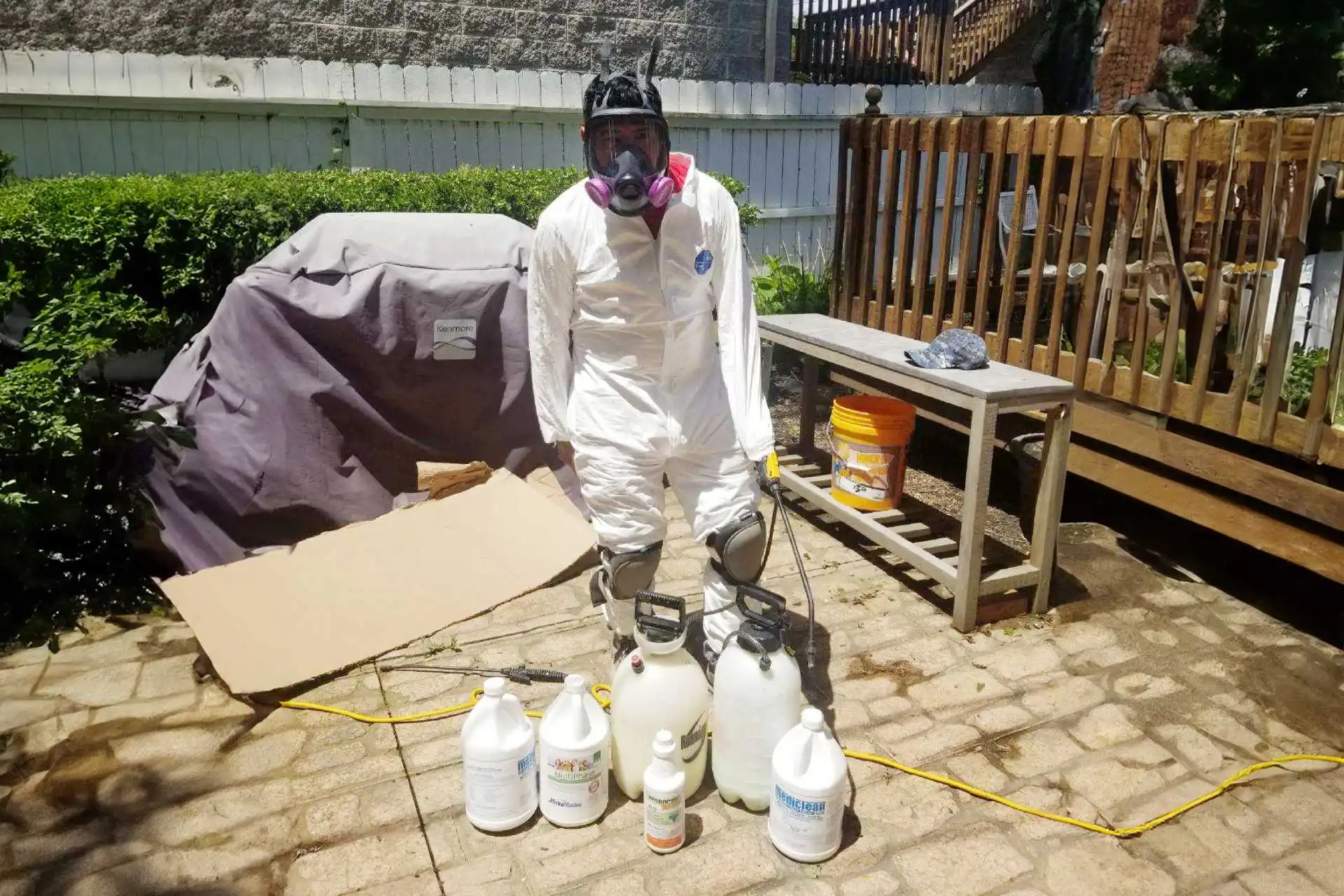 Worker in protective gear with chemical containers in outdoor setting