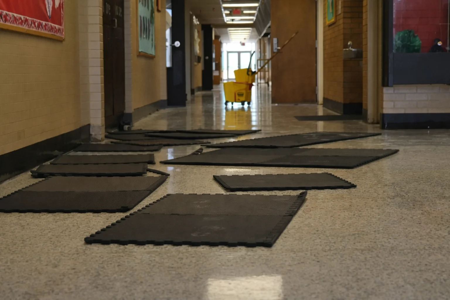 Scattered mats on a school hallway floor with cleaning cart
